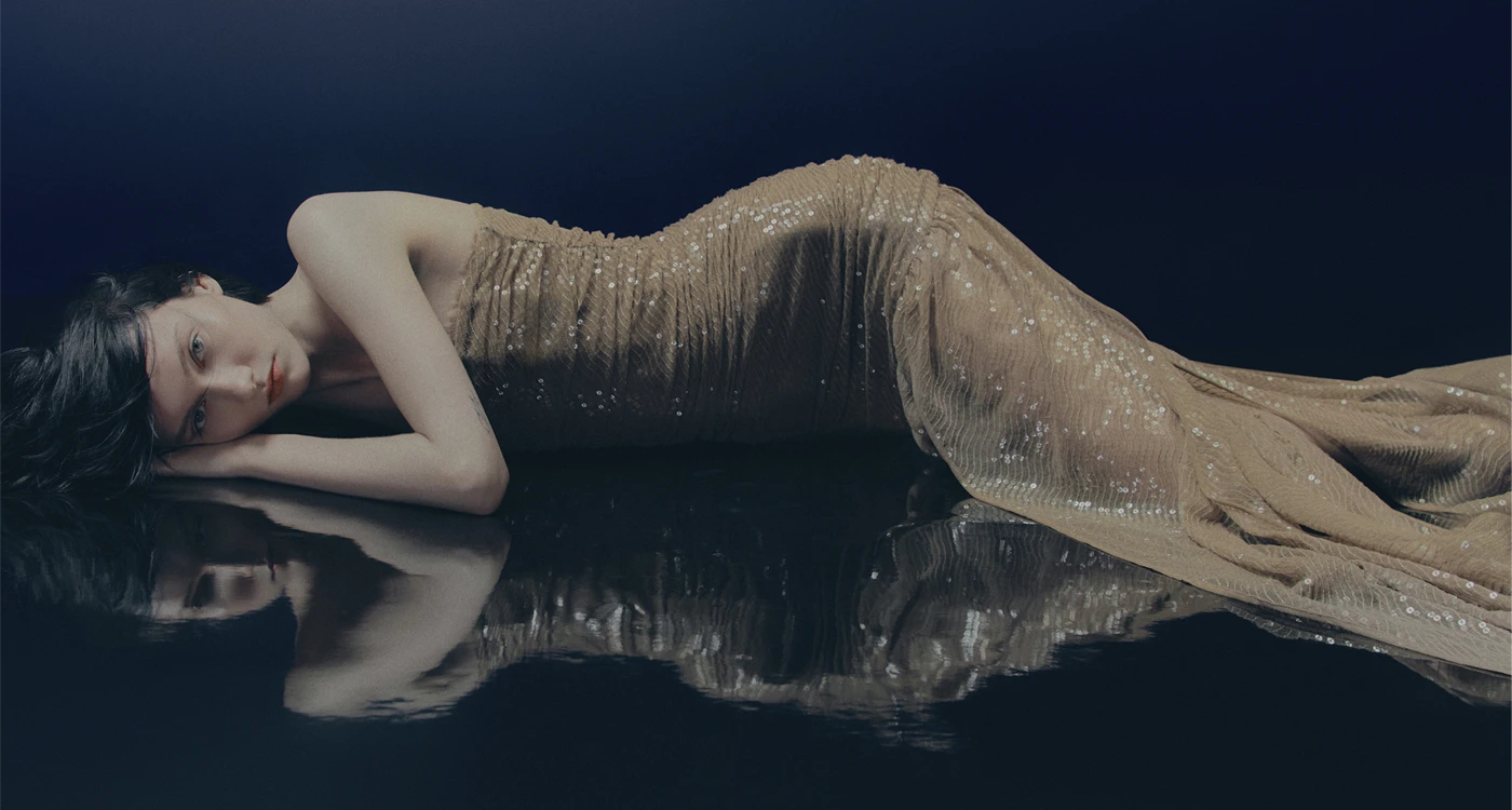 Model in H&M Studio Holiday 2025 collection wearing a dramatic sequinned dress with ruffles and lace detailing, styled in a moody, cinematic setting.